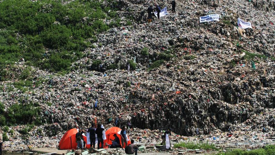 Beberapa aktivis lingkungan makan di dekat tenda mereka saat aksi damai di TPA Cipayung di Depok, Provinsi Jawa Barat Indonesia pada 31 Mei 2023. Aktivis lingkungan ambil bagian dalam aksi damai untuk menunjukkan meningkatnya penumpukan sampah yang melebihi kapasitas dan menyebabkan berbagai masalah kesehatan dan lingkungan di kota. (Eko Siswono Toyudho/Anadolu Agency via Getty Images)