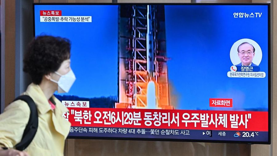 Seorang wanita berjalan melewati layar televisi yang menayangkan siaran berita dengan rekaman file peluncuran roket Korea Utara, di Stasiun Kereta Api Seoul di Seoul pada 31 Mei 2023. Korea Utara meluncurkan satelit mata-mata yang diklaim pada 31 Mei, kata militer Selatan, mendorong kebingungan di Seoul karena kota tersebut secara singkat mengeluarkan peringatan evakuasi karena kesalahan. (JUNG YEON-JE/AFP via Getty Images)