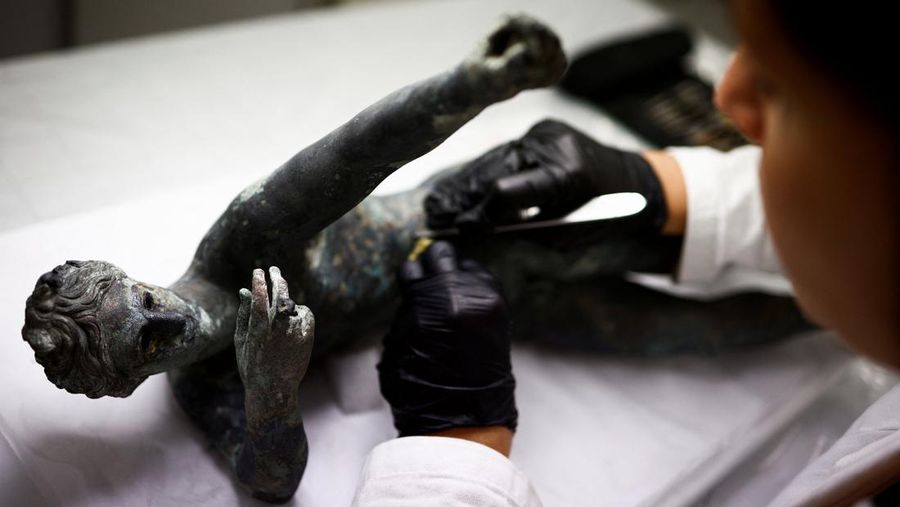 Sejumlah arkeolong memeriksa patung perunggu yang ditemukan di okasi pemandian kuno puncak bukit selatan di Grosseto, Italia. (REUTERS/GUGLIELMO MANGIAPANE)