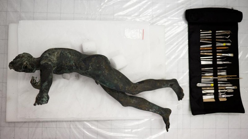 Sejumlah arkeolong memeriksa patung perunggu yang ditemukan di okasi pemandian kuno puncak bukit selatan di Grosseto, Italia. (REUTERS/GUGLIELMO MANGIAPANE)