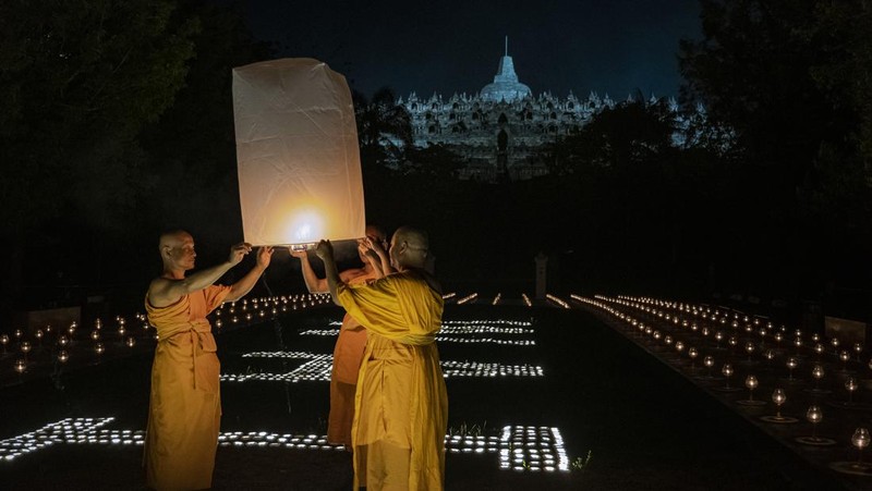 Umat Buddha dan turis melepaskan lampion ke udara di Candi Borobudur saat perayaan Hari Raya Waisak pada 4 Juni 2023 di Magelang, Jawa Tengah, Indonesia. Waisak dirayakan selama bulan purnama di bulan Mei atau Juni dengan upacara yang berpusat di sekitar tiga candi Budha, peziarah berjalan dari Mendut ke Pawon, berakhir di Borobudur. Hari suci merayakan kelahiran, pencerahan ke nirwana, dan meninggalnya Buddha Gautama, pendiri agama Buddha. (Ulet Ifansasti/Getty Images)