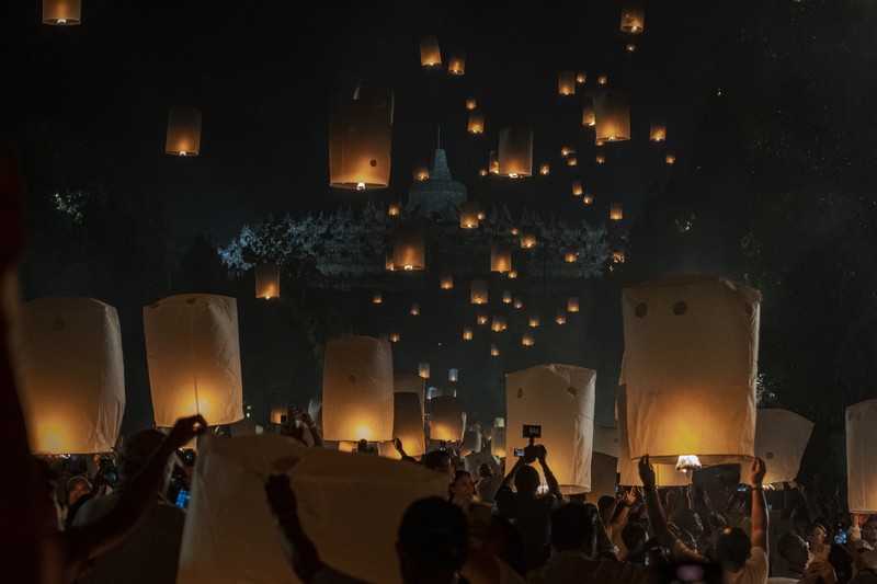 Umat Buddha dan turis melepaskan lampion ke udara di Candi Borobudur saat perayaan Hari Raya Waisak pada 4 Juni 2023 di Magelang, Jawa Tengah, Indonesia. Waisak dirayakan selama bulan purnama di bulan Mei atau Juni dengan upacara yang berpusat di sekitar tiga candi Budha, peziarah berjalan dari Mendut ke Pawon, berakhir di Borobudur. Hari suci merayakan kelahiran, pencerahan ke nirwana, dan meninggalnya Buddha Gautama, pendiri agama Buddha. (Ulet Ifansasti/Getty Images)