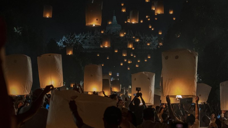 Umat Buddha dan turis melepaskan lampion ke udara di Candi Borobudur saat perayaan Hari Raya Waisak pada 4 Juni 2023 di Magelang, Jawa Tengah, Indonesia. Waisak dirayakan selama bulan purnama di bulan Mei atau Juni dengan upacara yang berpusat di sekitar tiga candi Budha, peziarah berjalan dari Mendut ke Pawon, berakhir di Borobudur. Hari suci merayakan kelahiran, pencerahan ke nirwana, dan meninggalnya Buddha Gautama, pendiri agama Buddha. (Ulet Ifansasti/Getty Images)