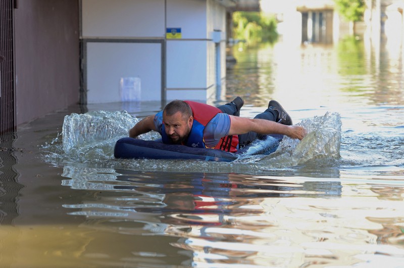 Tim penyelamat mengevakuasi seorang wanita dengan anjingnya di daerah banjir kota pada 7 Juni 2023 di Kherson, Ukraina. Akibat rusaknya bendungan Kakhovka, sekitar 80 pemukiman, termasuk Kherson, terancam banjir. Pihak berwenang dan sukarelawan mulai mengevakuasi penduduk dari daerah berbahaya. (Yan Dobronosov/Global Images Ukraine via Getty Images)