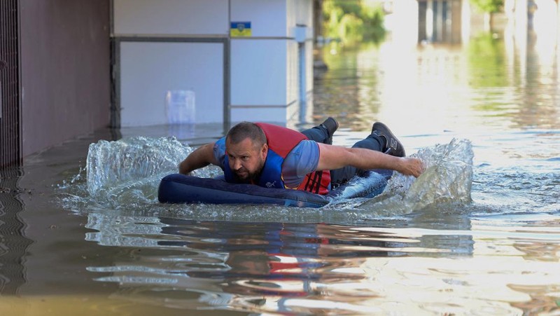 Tim penyelamat mengevakuasi seorang wanita dengan anjingnya di daerah banjir kota pada 7 Juni 2023 di Kherson, Ukraina. Akibat rusaknya bendungan Kakhovka, sekitar 80 pemukiman, termasuk Kherson, terancam banjir. Pihak berwenang dan sukarelawan mulai mengevakuasi penduduk dari daerah berbahaya. (Yan Dobronosov/Global Images Ukraine via Getty Images)
