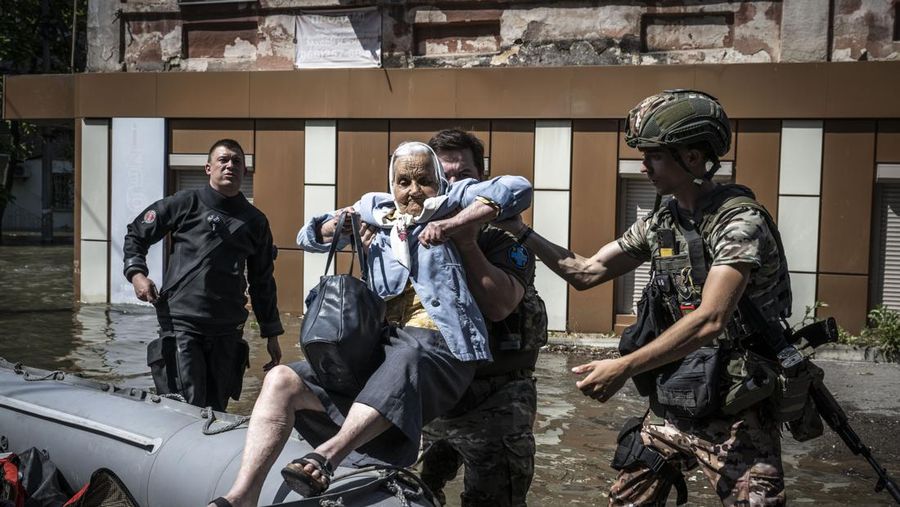 Tim penyelamat mengevakuasi seorang wanita dengan anjingnya di daerah banjir kota pada 7 Juni 2023 di Kherson, Ukraina. Akibat rusaknya bendungan Kakhovka, sekitar 80 pemukiman, termasuk Kherson, terancam banjir. Pihak berwenang dan sukarelawan mulai mengevakuasi penduduk dari daerah berbahaya. (Yan Dobronosov/Global Images Ukraine via Getty Images)