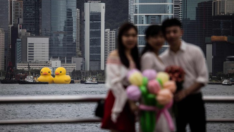 Seorang wanita berpose di depan dua bebek kuning tiup besar yang disebut 