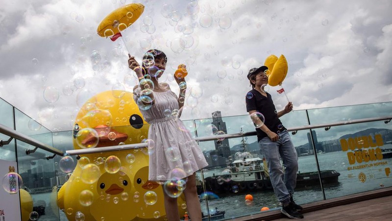 Seorang wanita berpose di depan dua bebek kuning tiup besar yang disebut 