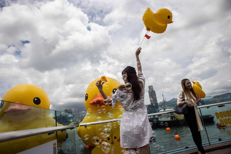 Seorang wanita berpose di depan dua bebek kuning tiup besar yang disebut 