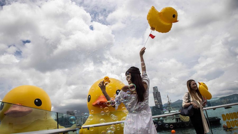 Seorang wanita berpose di depan dua bebek kuning tiup besar yang disebut 