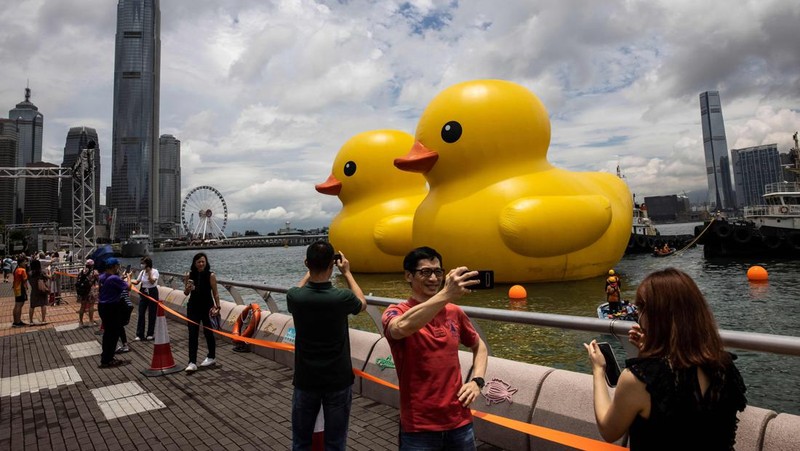 Seorang wanita berpose di depan dua bebek kuning tiup besar yang disebut 