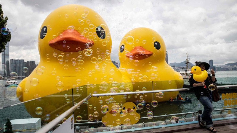Seorang wanita berpose di depan dua bebek kuning tiup besar yang disebut 