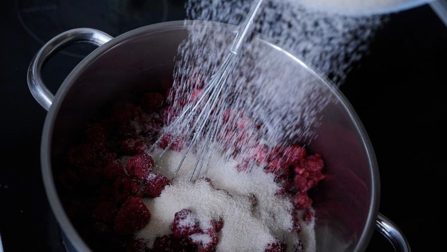 PRODUCTION - 17 April 2023, Berlin: A woman pours preserving sugar on raspberries, which are in a pot on the stove flame. Photo: Annette Riedl/dpa (Photo by Annette Riedl/picture alliance via Getty Images)