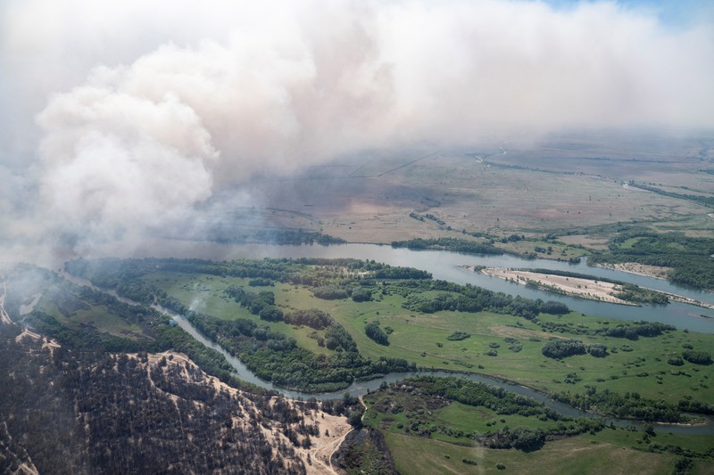 Sebuah helikopter terbang di tengah asap di atas sabuk hutan selama operasi untuk menahan kebakaran hutan di wilayah Abai timur, Kazakhstan, 12 Juni 2023. (REUTERS/Turar Kazangapov)