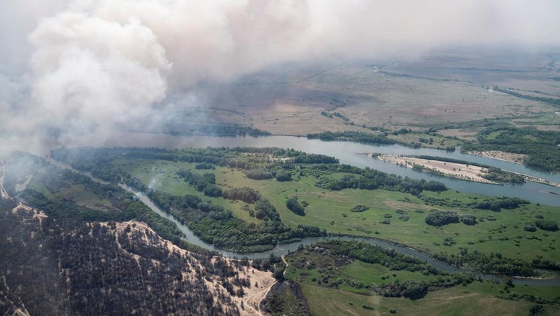 Sebuah helikopter terbang di tengah asap di atas sabuk hutan selama operasi untuk menahan kebakaran hutan di wilayah Abai timur, Kazakhstan, 12 Juni 2023. (REUTERS/Turar Kazangapov)