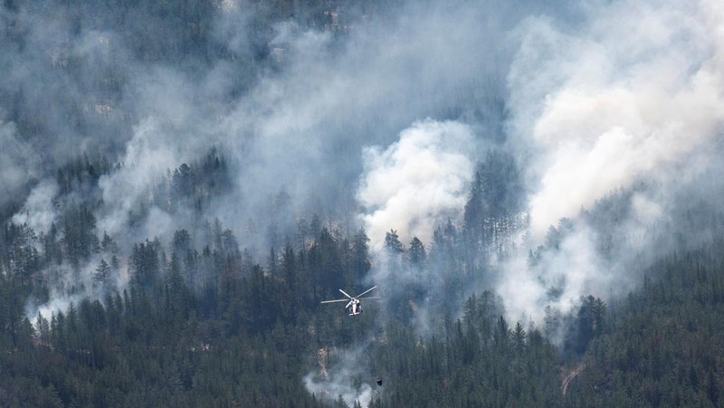 Sebuah helikopter terbang di tengah asap di atas sabuk hutan selama operasi untuk menahan kebakaran hutan di wilayah Abai timur, Kazakhstan, 12 Juni 2023. (REUTERS/Turar Kazangapov)