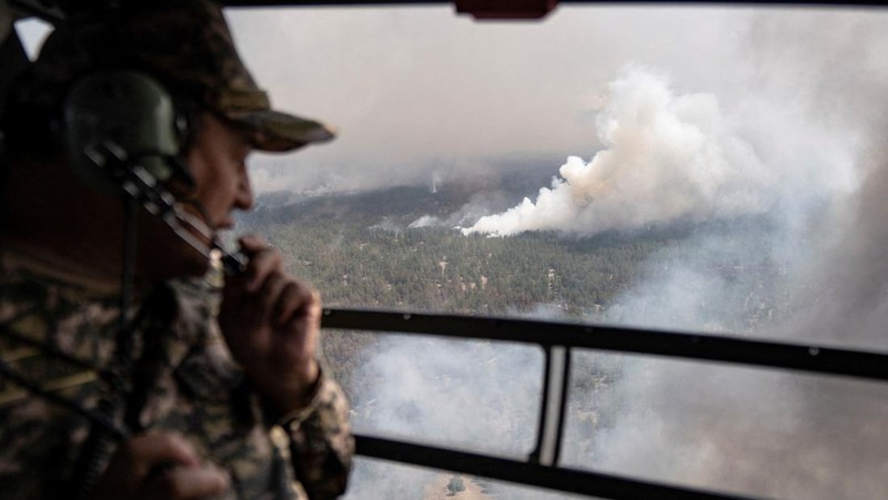 Sebuah helikopter terbang di tengah asap di atas sabuk hutan selama operasi untuk menahan kebakaran hutan di wilayah Abai timur, Kazakhstan, 12 Juni 2023. (REUTERS/Turar Kazangapov)