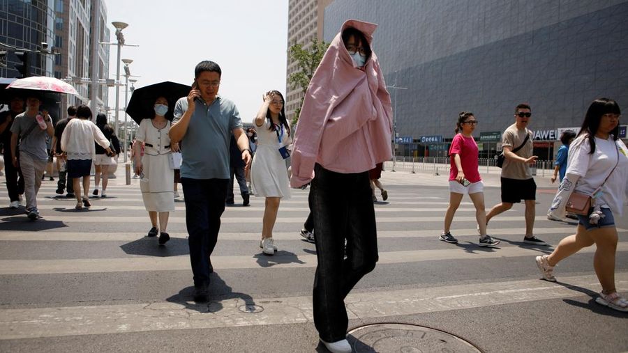 Seorang pejalan kaki melindungi dirinya dari sinar matahari saat melintasi jalan di hari yang panas di tengah peringatan oranye untuk gelombang panas, di Beijing, China 16 Juni 2023. (REUTERS/Florence Lo)