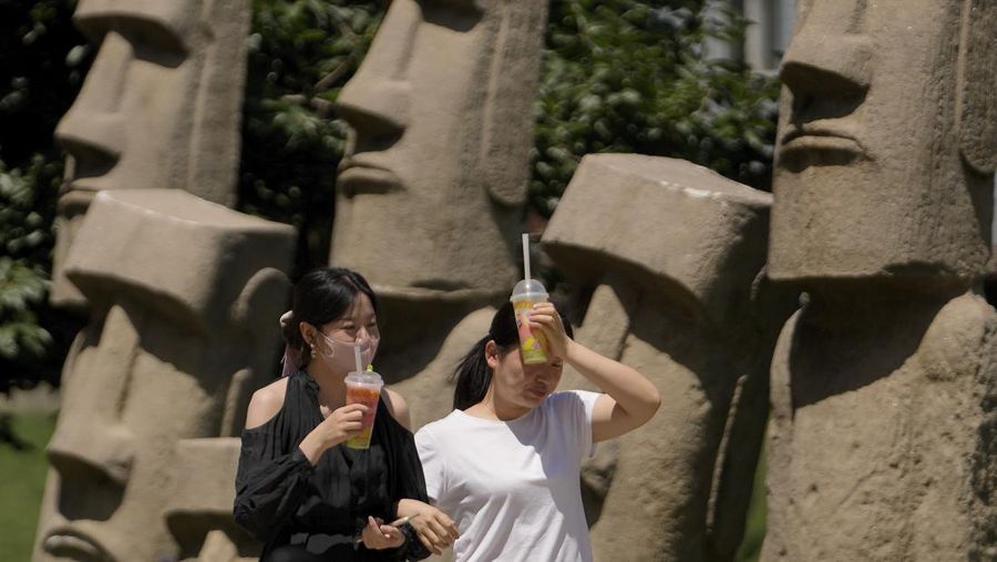 Seorang wanita meletakkan minuman dingin di dahinya untuk menenangkan diri saat dia berjalan dengan temannya di jalan pada hari yang panas di Beijing, Rabu (21/6/2023). (AP Photo/Andy Wong)