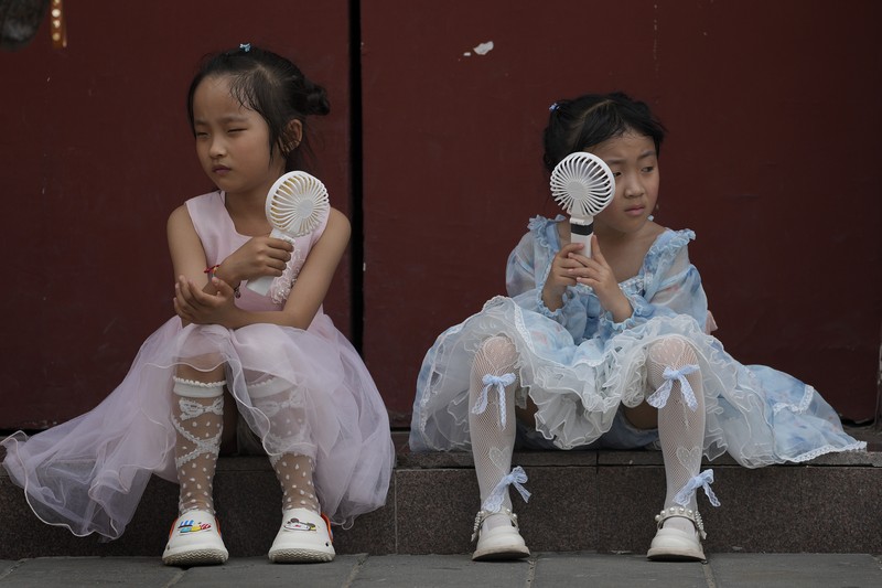 Anak-anak mendinginkan diri dengan kipas angin listrik saat beristirahat. (AP/Andy Wong)