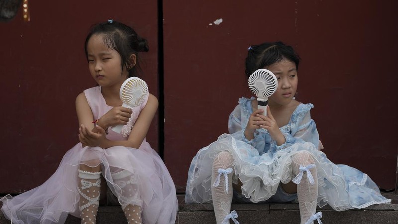Anak-anak mendinginkan diri dengan kipas angin listrik saat beristirahat. (AP/Andy Wong)