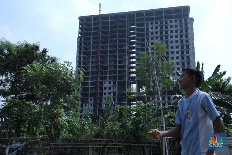 Warga melewati bangunan Apartemen Point 8 yang terbengkalai di kawasan Daan Mogot, Jakarta, Selasa (27/6/2023). (CNBC Indonesia/Tri Susilo)