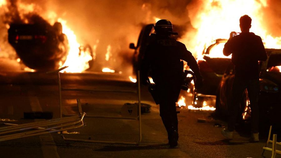 Petugas pemadam kebakaran berdiri saat mereka memadamkan kendaraan yang terbakar selama bentrokan antara pengunjuk rasa dan polisi, setelah kematian Nahel, seorang remaja berusia 17 tahun yang dibunuh oleh seorang petugas polisi Prancis saat menghentikan lalu lintas, di Nanterre, pinggiran kota Paris, Prancis, 28 Juni 2023. (REUTERS/Stephanie Lecocq)