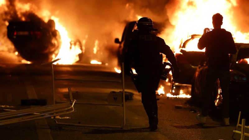 Petugas pemadam kebakaran berdiri saat mereka memadamkan kendaraan yang terbakar selama bentrokan antara pengunjuk rasa dan polisi, setelah kematian Nahel, seorang remaja berusia 17 tahun yang dibunuh oleh seorang petugas polisi Prancis saat menghentikan lalu lintas, di Nanterre, pinggiran kota Paris, Prancis, 28 Juni 2023. (REUTERS/Stephanie Lecocq)