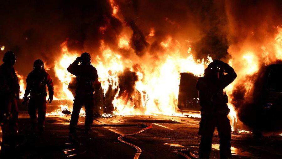 Petugas pemadam kebakaran berdiri saat mereka memadamkan kendaraan yang terbakar selama bentrokan antara pengunjuk rasa dan polisi, setelah kematian Nahel, seorang remaja berusia 17 tahun yang dibunuh oleh seorang petugas polisi Prancis saat menghentikan lalu lintas, di Nanterre, pinggiran kota Paris, Prancis, 28 Juni 2023. (REUTERS/Stephanie Lecocq)