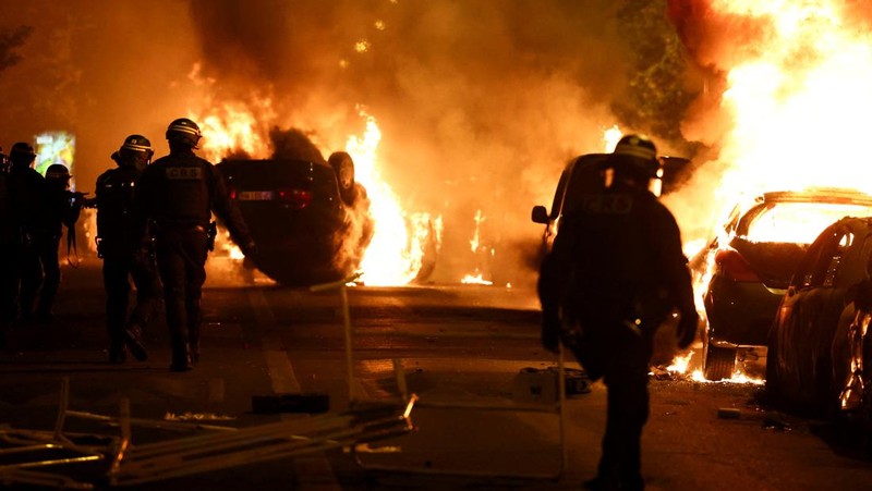 Petugas pemadam kebakaran berdiri saat mereka memadamkan kendaraan yang terbakar selama bentrokan antara pengunjuk rasa dan polisi, setelah kematian Nahel, seorang remaja berusia 17 tahun yang dibunuh oleh seorang petugas polisi Prancis saat menghentikan lalu lintas, di Nanterre, pinggiran kota Paris, Prancis, 28 Juni 2023. (REUTERS/Stephanie Lecocq)