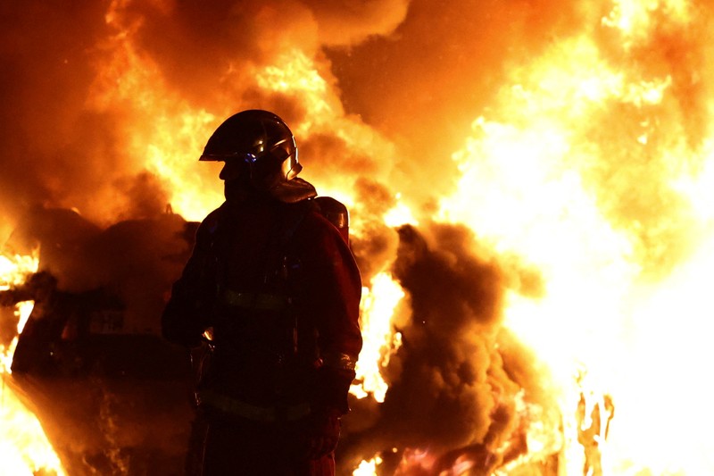 Petugas pemadam kebakaran berdiri saat mereka memadamkan kendaraan yang terbakar selama bentrokan antara pengunjuk rasa dan polisi, setelah kematian Nahel, seorang remaja berusia 17 tahun yang dibunuh oleh seorang petugas polisi Prancis saat menghentikan lalu lintas, di Nanterre, pinggiran kota Paris, Prancis, 28 Juni 2023. (REUTERS/Stephanie Lecocq)