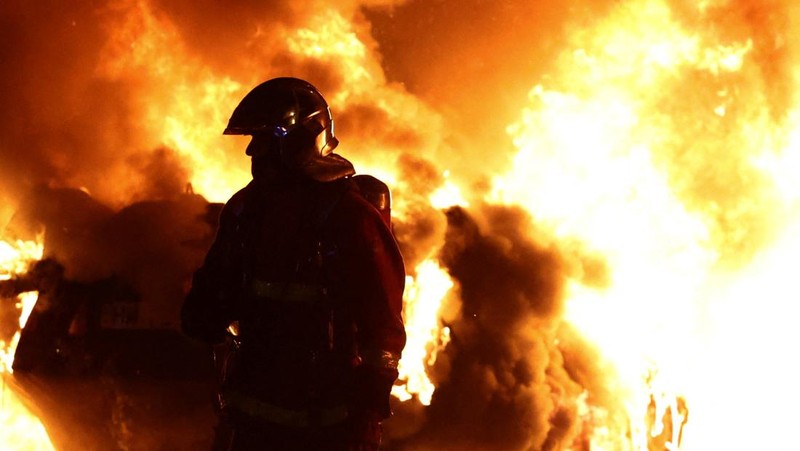 Petugas pemadam kebakaran berdiri saat mereka memadamkan kendaraan yang terbakar selama bentrokan antara pengunjuk rasa dan polisi, setelah kematian Nahel, seorang remaja berusia 17 tahun yang dibunuh oleh seorang petugas polisi Prancis saat menghentikan lalu lintas, di Nanterre, pinggiran kota Paris, Prancis, 28 Juni 2023. (REUTERS/Stephanie Lecocq)