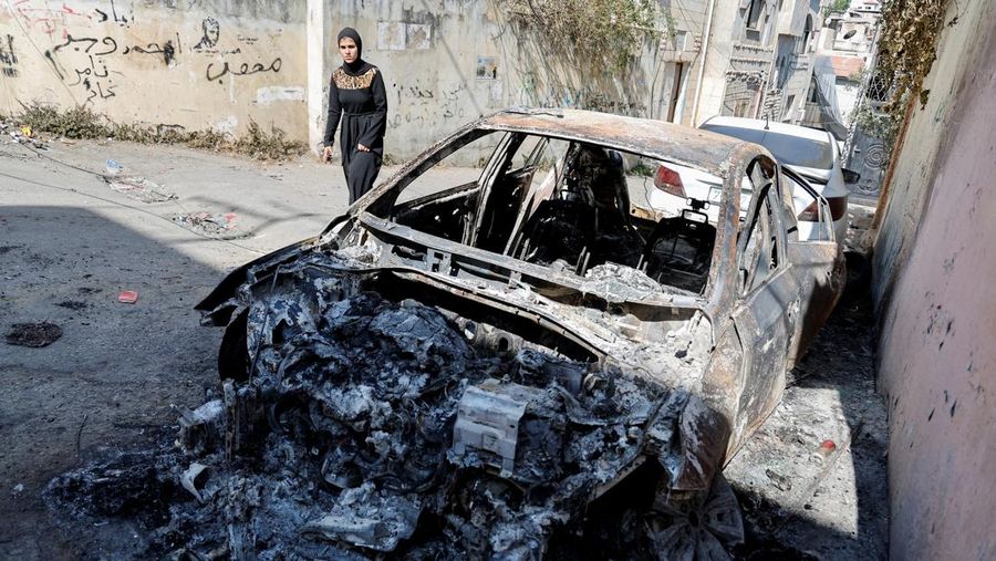 Seorang wanita Palestina berjalan melewati reruntuhan kendaraan setelah operasi militer Israel, di Jenin di Tepi Barat yang diduduki Israel 5 Juli 2023. (REUTERS/Raneen Sawafta)