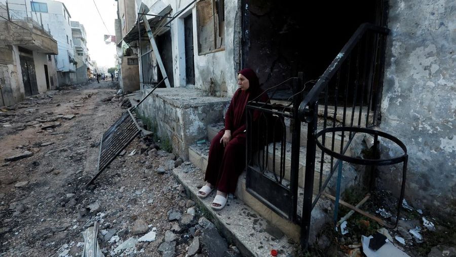 Seorang wanita Palestina duduk di depan sebuah bangunan yang rusak setelah penarikan tentara Israel dari kamp Jenin, di Jenin, di Tepi Barat yang diduduki Israel 5 Juli 2023. (REUTERS/Mohamad Torokman)