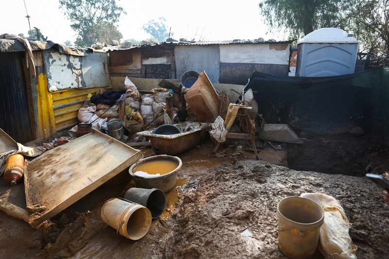 Seorang polisi dan anggota tim forensik memeriksa lokasi dugaan kebocoran gas yang diduga terkait dengan penambangan ilegal, di pemukiman gubuk Angelo, dekat Boksburg, timur Johannesburg, Afrika Selatan, 6 Juli 2023. (REUTERS/Siphiwe Sibeko)