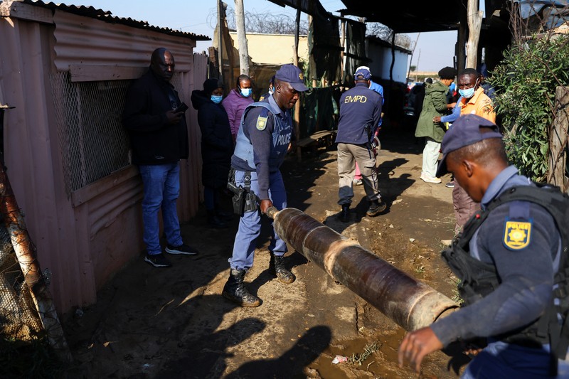 Seorang polisi dan anggota tim forensik memeriksa lokasi dugaan kebocoran gas yang diduga terkait dengan penambangan ilegal, di pemukiman gubuk Angelo, dekat Boksburg, timur Johannesburg, Afrika Selatan, 6 Juli 2023. (REUTERS/Siphiwe Sibeko)