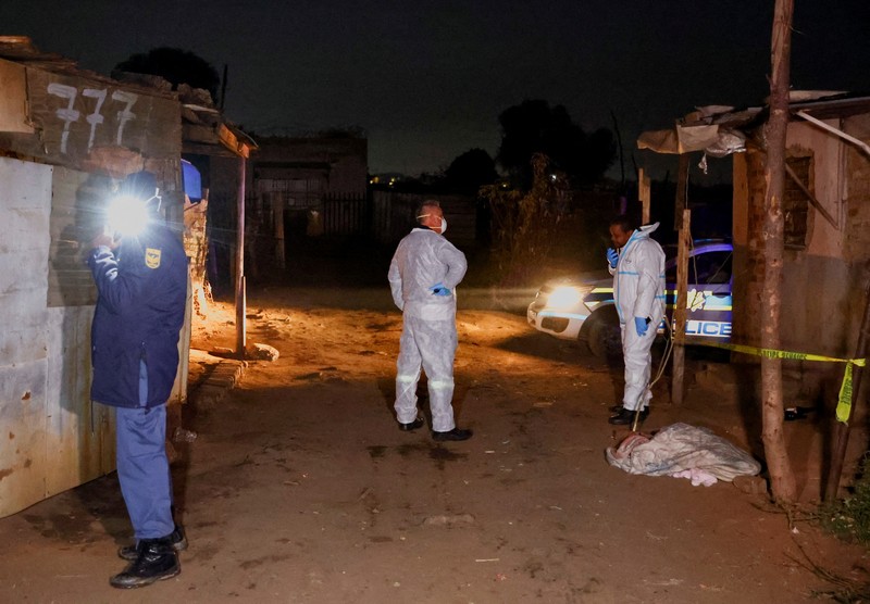 Seorang polisi dan anggota tim forensik memeriksa lokasi dugaan kebocoran gas yang diduga terkait dengan penambangan ilegal, di pemukiman gubuk Angelo, dekat Boksburg, timur Johannesburg, Afrika Selatan, 6 Juli 2023. (REUTERS/Siphiwe Sibeko)