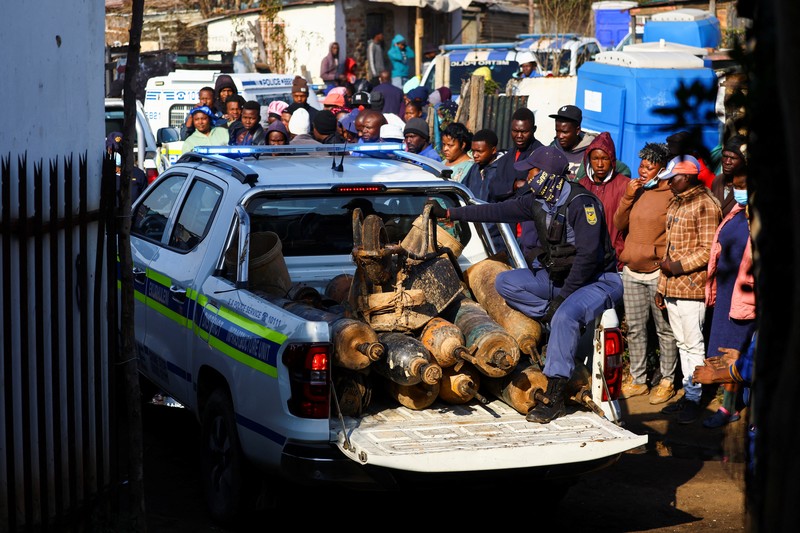 Seorang polisi dan anggota tim forensik memeriksa lokasi dugaan kebocoran gas yang diduga terkait dengan penambangan ilegal, di pemukiman gubuk Angelo, dekat Boksburg, timur Johannesburg, Afrika Selatan, 6 Juli 2023. (REUTERS/Siphiwe Sibeko)
