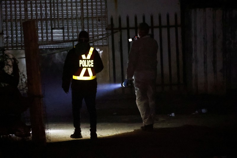 Seorang polisi dan anggota tim forensik memeriksa lokasi dugaan kebocoran gas yang diduga terkait dengan penambangan ilegal, di pemukiman gubuk Angelo, dekat Boksburg, timur Johannesburg, Afrika Selatan, 6 Juli 2023. Seorang polisi dan anggota tim forensik memeriksa lokasi dugaan kebocoran gas yang diduga terkait dengan penambangan ilegal, di pemukiman gubuk Angelo, dekat Boksburg, timur Johannesburg, Afrika Selatan, 6 Juli 2023. (REUTERS/Siphiwe Sibeko)