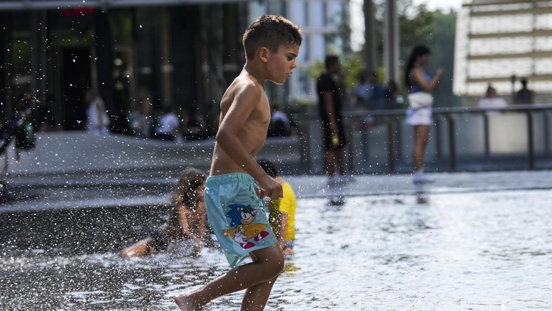 Seorang pria bernama David memeriksa ponselnya saat dia berdiri di dekat kipas angin untuk mendinginkan diri, selama gelombang panas di seluruh Italia, di Roma, 14 Juli 2023. (REUTERS/Guglielmo Mangiapane)