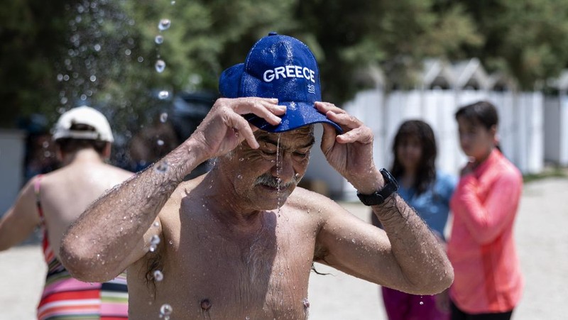 Seorang pria bernama David memeriksa ponselnya saat dia berdiri di dekat kipas angin untuk mendinginkan diri, selama gelombang panas di seluruh Italia, di Roma, 14 Juli 2023. (REUTERS/Guglielmo Mangiapane)