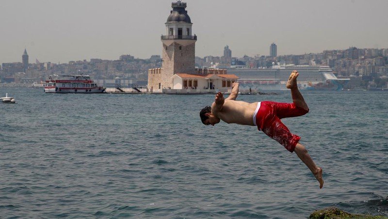 Seorang pria bernama David memeriksa ponselnya saat dia berdiri di dekat kipas angin untuk mendinginkan diri, selama gelombang panas di seluruh Italia, di Roma, 14 Juli 2023. (REUTERS/Guglielmo Mangiapane)
