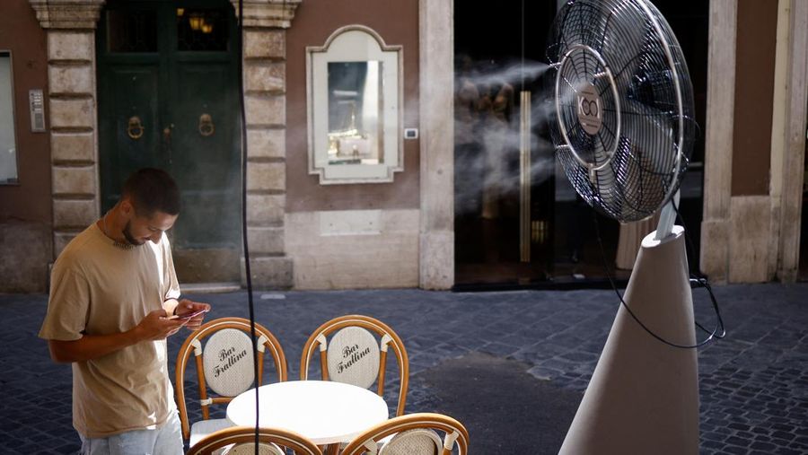 Seorang pria bernama David memeriksa ponselnya saat dia berdiri di dekat kipas angin untuk mendinginkan diri, selama gelombang panas di seluruh Italia, di Roma, 14 Juli 2023. (REUTERS/Guglielmo Mangiapane)