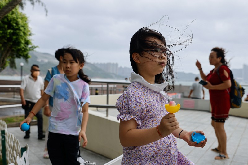 Hong Kong Typhoon Mainland Chinese tourists run along a promenade during a typhoon in Hong Kong, Monday, July 17, 2023. Schools and the stock market were closed in Hong Kong on Monday as Typhoon Talim swept south of the city. (AP Photo/Louise Delmotte)