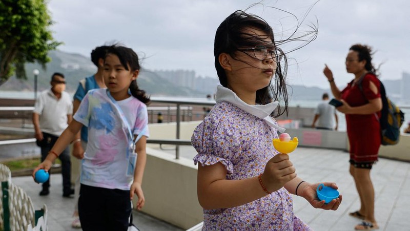 Mainland Chinese tourists run along a promenade during a typhoon in Hong Kong, Monday, July 17, 2023. Schools and the stock market were closed in Hong Kong on Monday as Typhoon Talim swept south of the city. (AP Photo/Louise Delmotte)