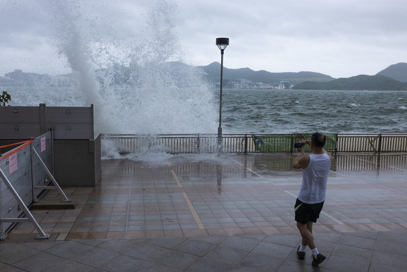 Mainland Chinese tourists run along a promenade during a typhoon in Hong Kong, Monday, July 17, 2023. Schools and the stock market were closed in Hong Kong on Monday as Typhoon Talim swept south of the city. (AP Photo/Louise Delmotte)