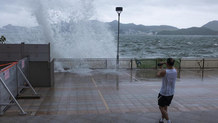 Mainland Chinese tourists run along a promenade during a typhoon in Hong Kong, Monday, July 17, 2023. Schools and the stock market were closed in Hong Kong on Monday as Typhoon Talim swept south of the city. (AP Photo/Louise Delmotte)