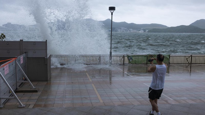 Mainland Chinese tourists run along a promenade during a typhoon in Hong Kong, Monday, July 17, 2023. Schools and the stock market were closed in Hong Kong on Monday as Typhoon Talim swept south of the city. (AP Photo/Louise Delmotte)