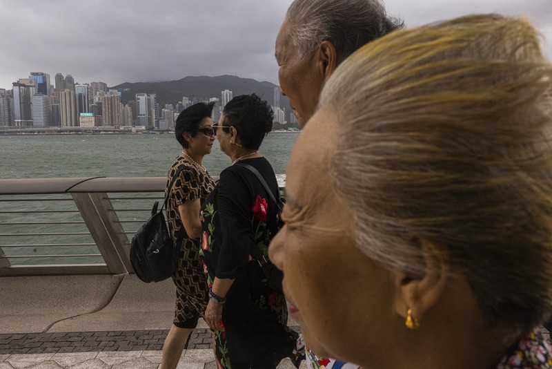 Mainland Chinese tourists run along a promenade during a typhoon in Hong Kong, Monday, July 17, 2023. Schools and the stock market were closed in Hong Kong on Monday as Typhoon Talim swept south of the city. (AP Photo/Louise Delmotte)