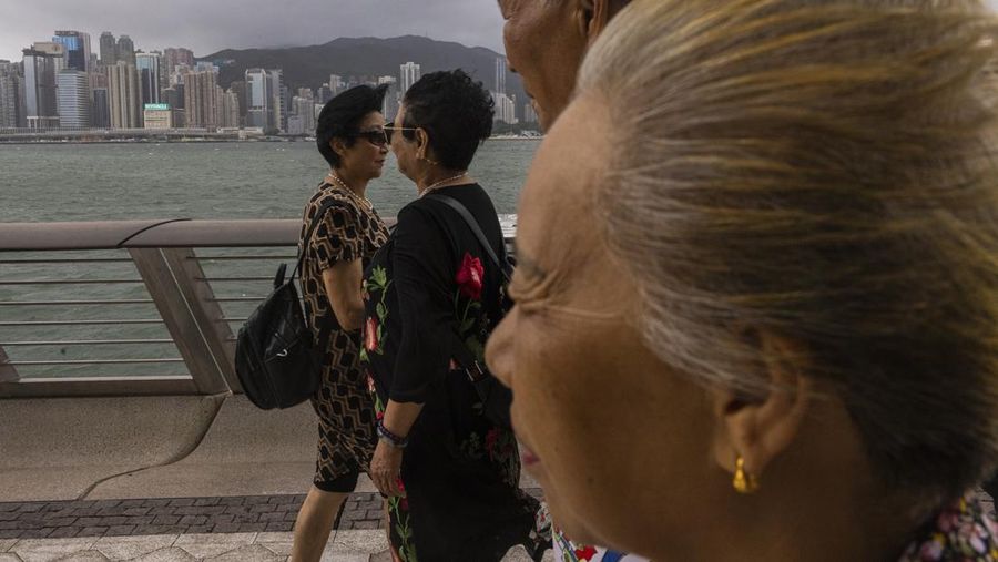 Mainland Chinese tourists run along a promenade during a typhoon in Hong Kong, Monday, July 17, 2023. Schools and the stock market were closed in Hong Kong on Monday as Typhoon Talim swept south of the city. (AP Photo/Louise Delmotte)